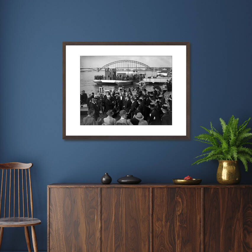 Zwart-witfoto van een carnavalsplechtigheid op de Waalkade in Nijmegen met de Waalbrug op de achtergrond. – donkerbruine wissellijst in woonkamer