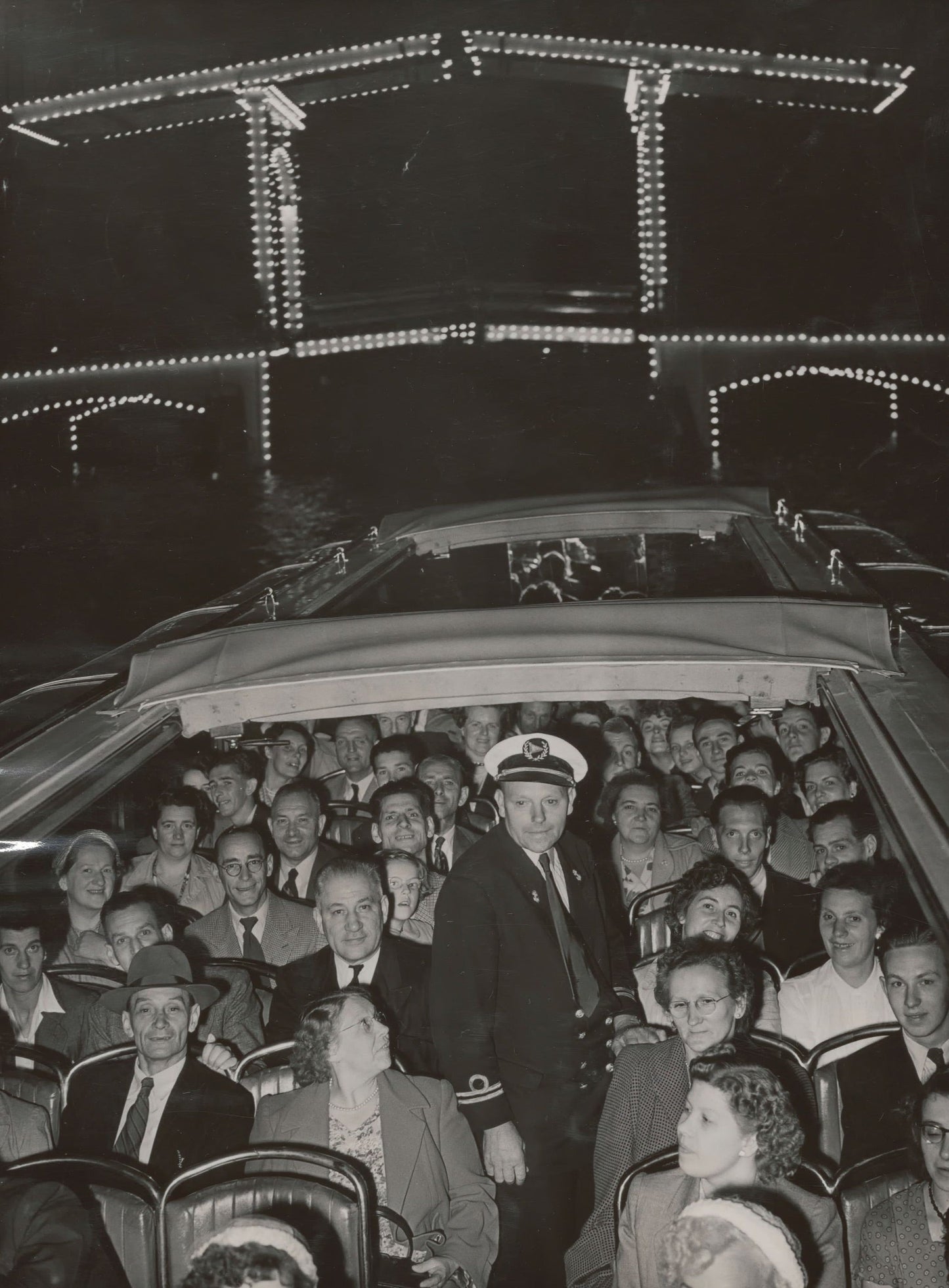 Zwart-witfoto uit 1953 van de verlichte Magere Brug over de Amstel in Amsterdam met een rondvaartboot.