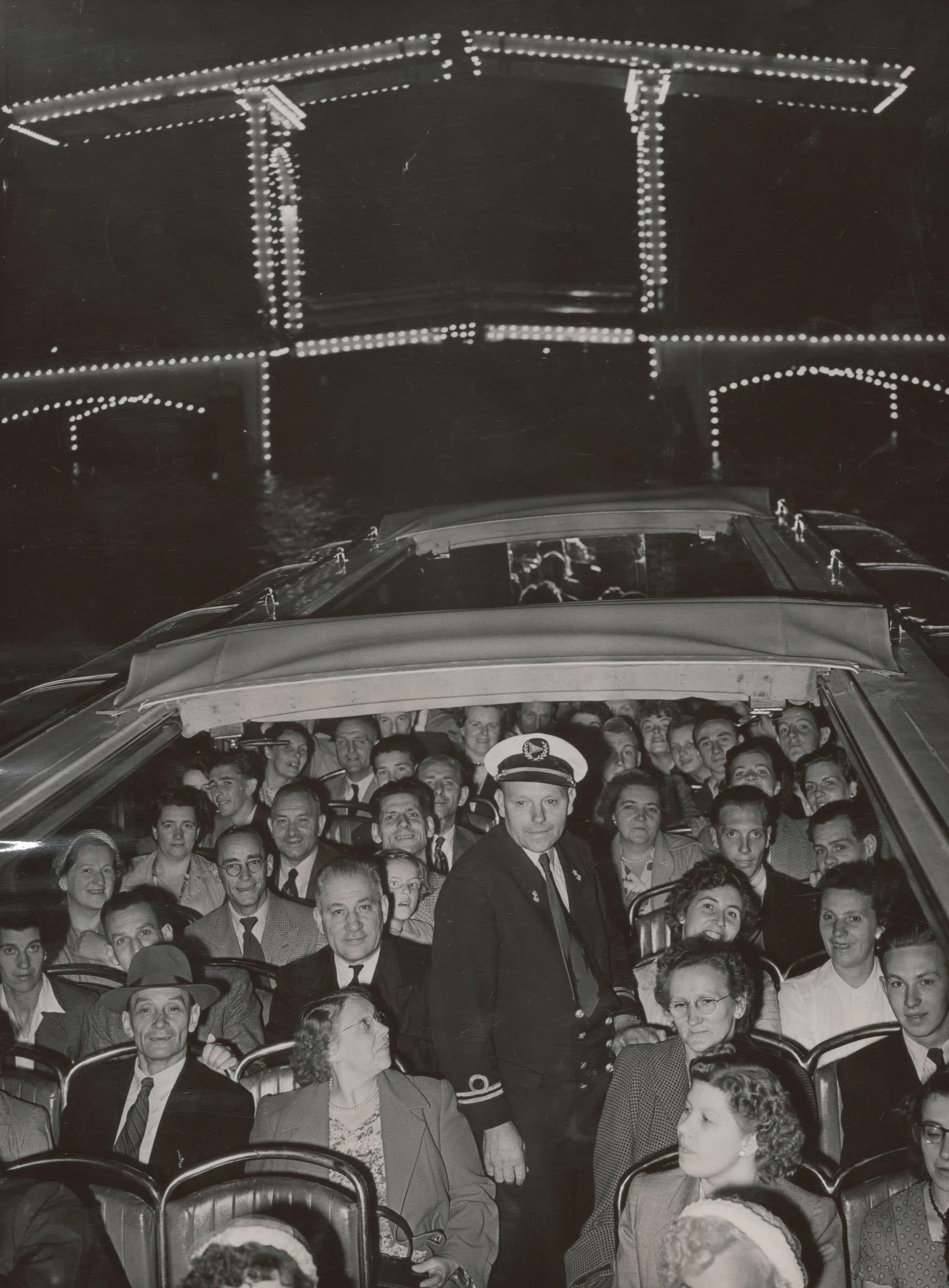 Zwart-witfoto uit 1953 van de verlichte Magere Brug over de Amstel in Amsterdam met een rondvaartboot.