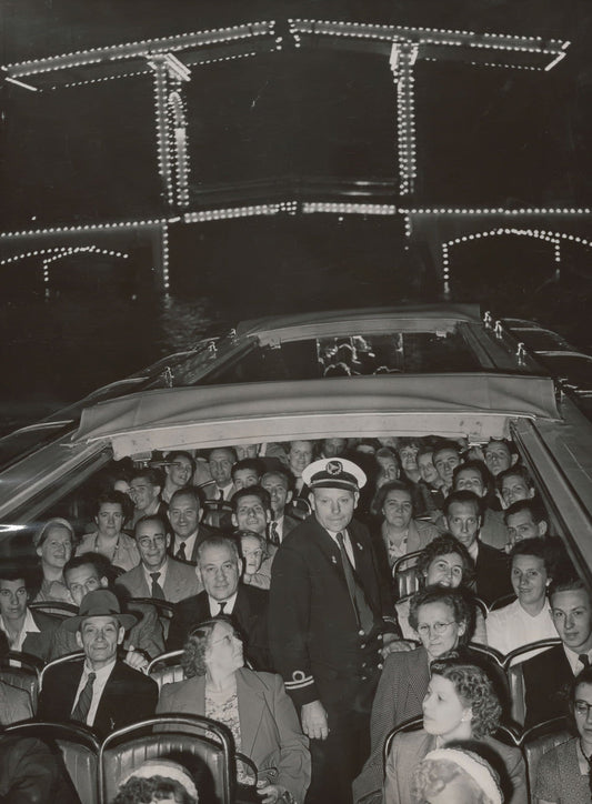 Zwart-witfoto uit 1953 van de verlichte Magere Brug over de Amstel in Amsterdam met een rondvaartboot.