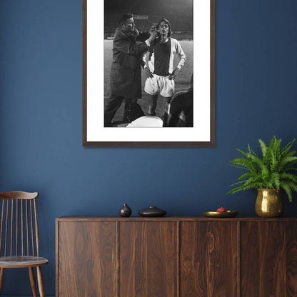 Zwart-witfoto uit 1971 van Johan Cruijff die wordt verzorgd door Ajax-clubarts Rolink in Amsterdam. – donkerbruine wissellijst in woonkamer