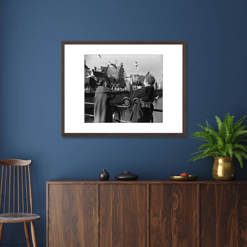 Zwart-witfoto uit 1954 van cineast Herman van der Horst die een vrouw filmt die meeuwen voert in Den Haag. – donkerbruine wissellijst in woonkamer