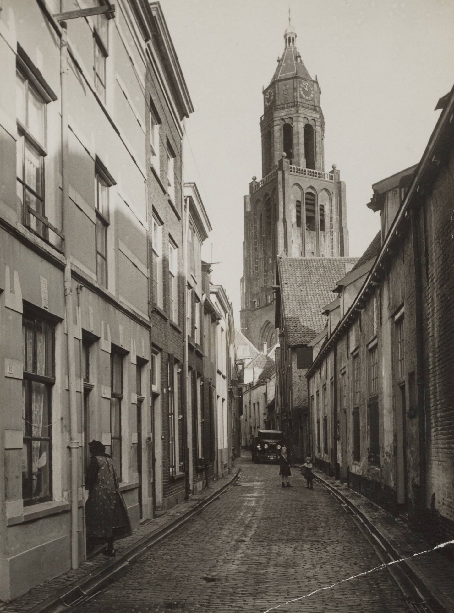 Zwart-witfoto van de Trompetsteeg in Arnhem met zicht op de toren van de Grote Kerk.